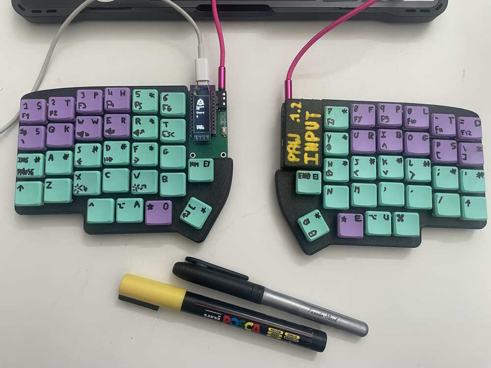 the keyboard in all its glory, with hand-written keycap lettering and the beautiful therian logo on the info screen. some keycaps are purple (following the steno layout) and some are green